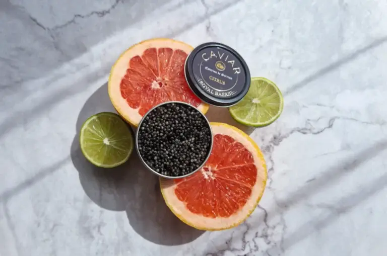Caviar tin surrounded by sliced grapefruit and lime on a marble surface.